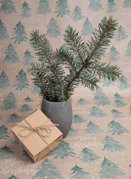 Ramo de abeto em vaso cinza e caixa de presente Xmas DIY em papel de embrulho festivo com abetos e inscrições Feliz Natal. — Fotografia de Stock