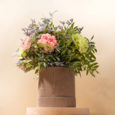 Çevre dostu kompozisyon, üzerinde çiçek buketi olan DIY karton vazo bej arka plandaki ahşap yuvarlak ayakta duruyor. Hygge tarzında modern kutlama kartı. Kare fotoğraf.