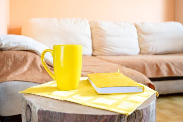 Trendy minimal home cozy interior with light corner sofa, creative wooden stump as table with yellow cup and notepad.