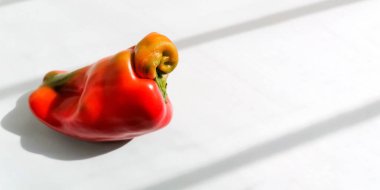 Beyaz zemin üzerinde çirkin bir turuncu biber ve son moda gölgeler. Taze sağlıklı organik sebzeler. Sıfır atık gıda konsepti olan pankart. Makul tüketim. Uzayı kopyala Seçici odak.