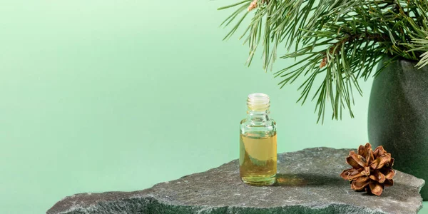 Glass bottle of essential pine oil on grey stone on mint green. Advertising banner. — Stock Photo, Image