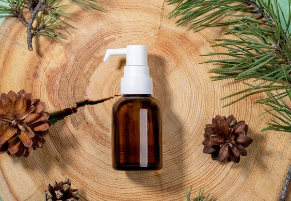 Small glass bottle with dispenser of spa aromatic essential pine oil, green branches, cones on wooden saw cut close up. — Stock Photo, Image