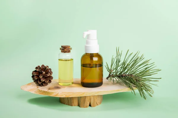 Small glass bottles with essential pine oil, green twig, cone on wooden saw cuts on mint green. — Stock Photo, Image