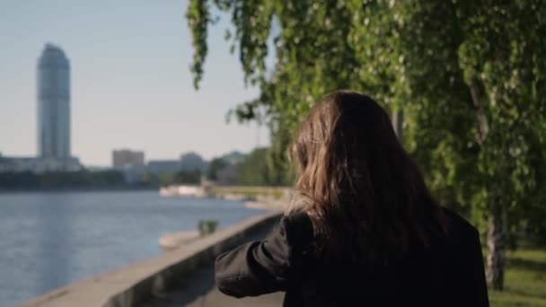 Жінка поспішає на роботу по парку вздовж міської набережної — стокове відео