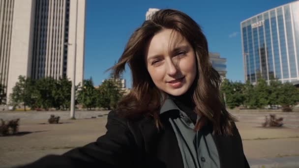Söt flicka filmar sig själv och vinkar till kameran stadsbilden i bakgrunden — Stockvideo