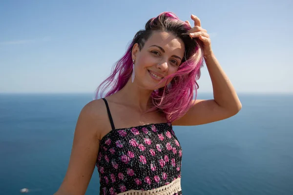 Fotoğrafta pembe saçlı, çiçekli bir elbisesi olan genç bir kadın var.
