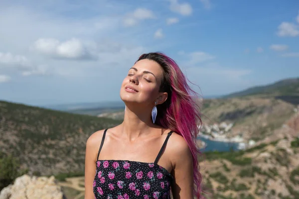 Çiçekli elbiseli, pembe saçlı, gülümseyen kız parlayan güneşin tadını çıkarıyor.