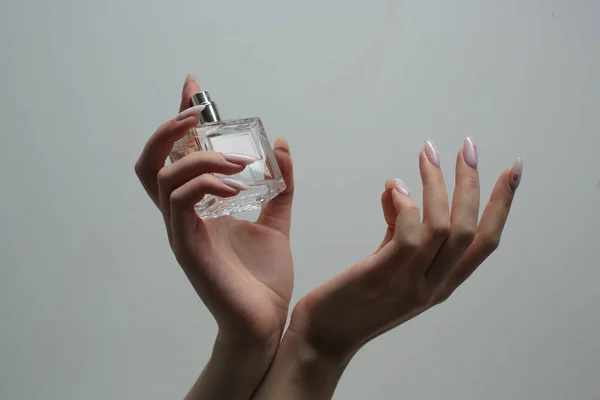 Las manos con manicuras sostienen una botella de perfume. Primer plano — Foto de Stock