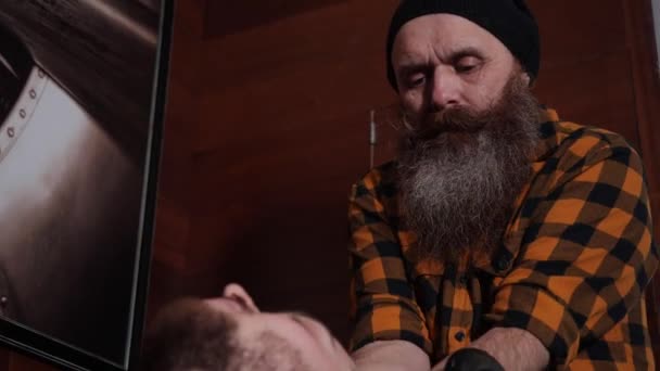 Een oude kapper met een lange baard wast het hoofd van een jonge klant in de gootsteen — Stockvideo