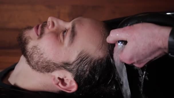 Перукаря миє голову молодого щасливого клієнта в перукарні. — стокове відео