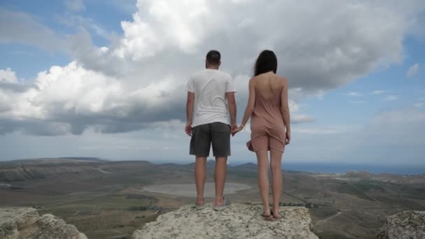 Ett ungt par står på toppen av ett berg och håller händer — Stockvideo