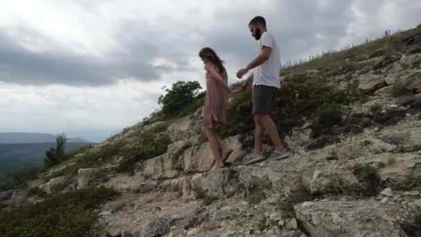 Um jovem casal de mãos dadas caminha ao longo do terreno montanhoso até a encosta — Vídeo de Stock