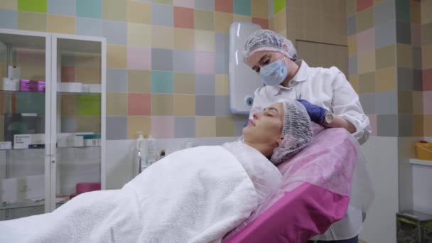A kozmetikus a fiatal nők arcát törli, mielőtt töltőanyag injekciót kapna. — Stock videók