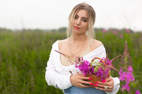 Mooi meisje in een wit shirt met een roze manicure staat in het veld holding — Stockfoto