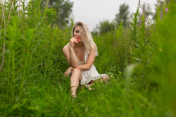Sexy jong meisje met rode lippenstift en zomer jurk zit tussen de hoge groene — Stockfoto