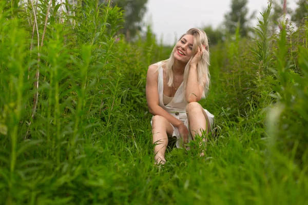Яскрава дівчина в літньому вбранні сидить серед високої трави в літню погоду — стокове фото