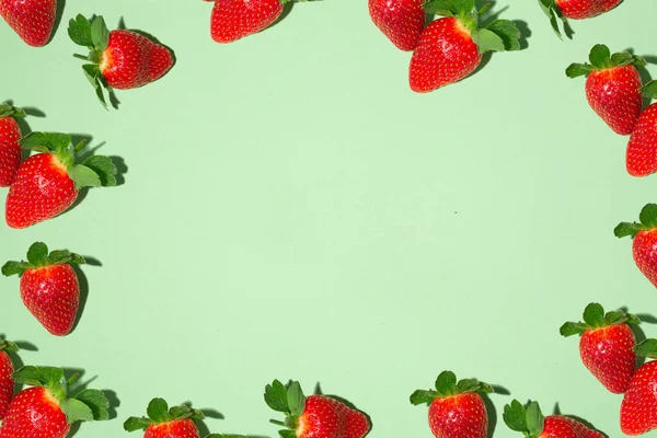 Cadre avec des fraises rouges juteuses sur un fond vert. Impression de fruits. — Photo