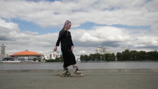 Bright young girl with long colored pigtails in a dress skates around the city — Stock Video