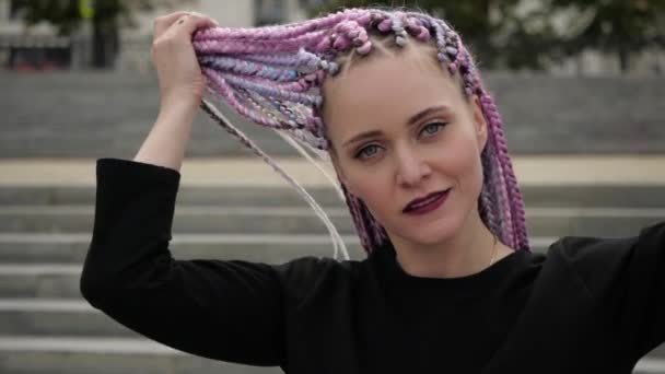 Незвичайна молода жінка з кольоровими кісками загадково дивиться в камеру — стокове відео