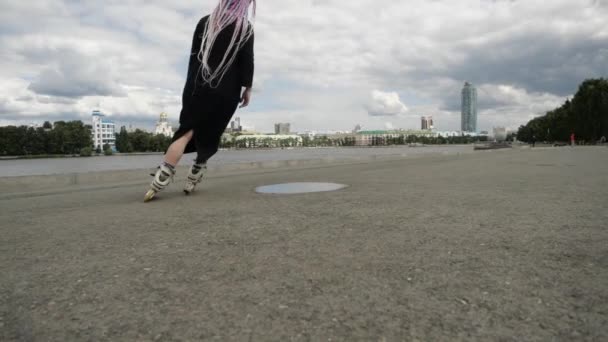 Яркая молодая женщина с косичками и в платье выполняет трюки на роликовых коньках — стоковое видео