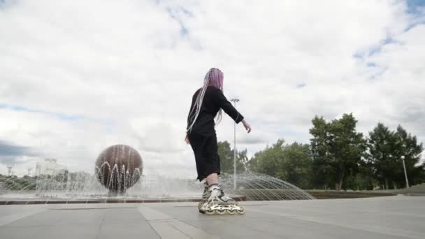 街中で黒いロングドレスのスケートをしている面白い若い女性 — ストック動画