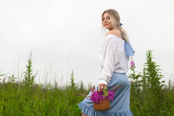 A young woman in a blue skirt and white blouse walks on a summer field