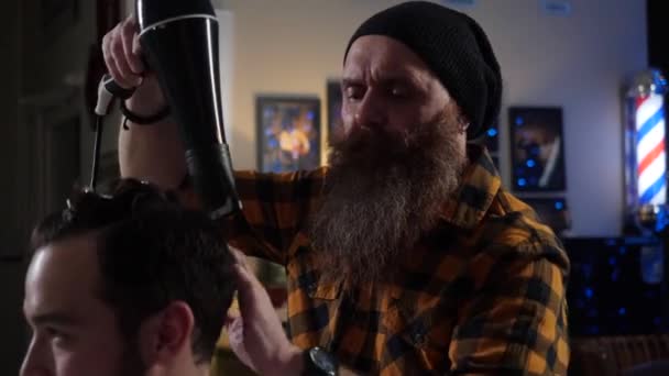 Vuxen man frisör med långt skägg torkar med en hårtork och sätter hår — Stockvideo