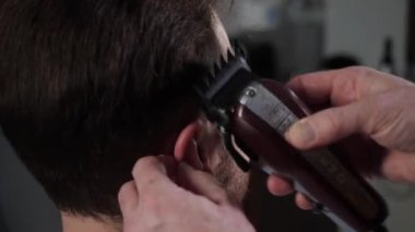Bir berberin eli traş makinesiyle saç kesimi şakakları yapar.