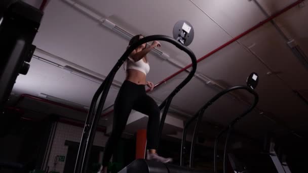 Спортивная девушка в белых топах и черных леггинсах бегает по беговой дорожке в спортзале — стоковое видео
