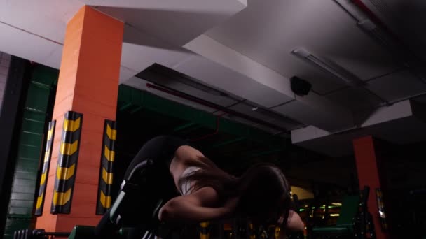 Chica en una parte superior realiza ejercicio de hiperextensión acostado en un simulador en un gimnasio — Vídeo de stock