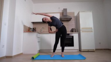 Enerjik esmer kız mutfaktaki paspasın üzerinde egzersiz yapıyor.