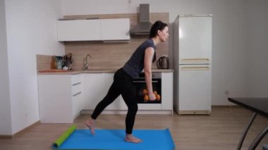 Genç bir kızın, dambılı mavi yoga minderinde egzersiz yapması. 