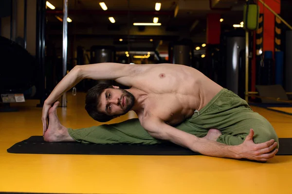 Genç bir erkek sporcu elini siyah bir paspasa dayayarak yoga yapıyor.