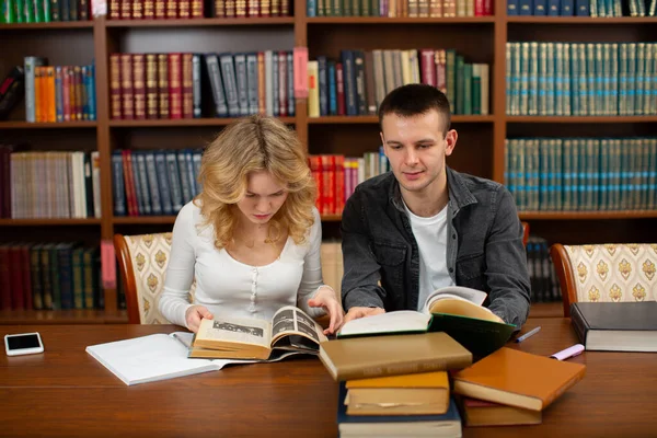 Üniversite öğrencileri kütüphanede oturup kitap okuyor ve sınava hazırlanıyorlar.