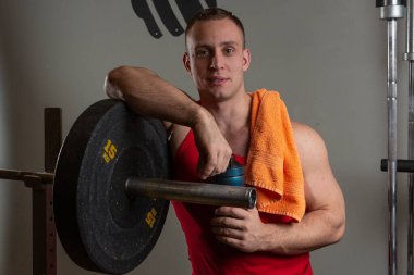 Spor salonunda simülatöre yaslanmış bir erkek kameraya gülümsüyor.