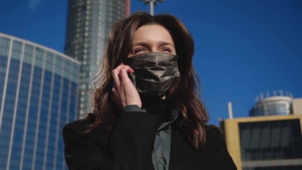 Chica con chaqueta y antibacteriana máscara se para en la calle habla por teléfono — Vídeos de Stock