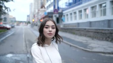 Bej kapüşonlu genç bir esmer kız kameraya bakar ve gülümser.