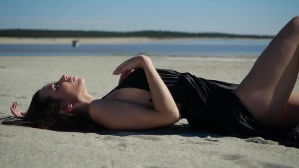 View from the side of an attractive girl posing for the camera lying on the sand — Stock Video