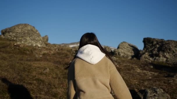 Une fille vêtue d'une veste beige et d'une veste à capuche se promène haut dans les montagnes — Video