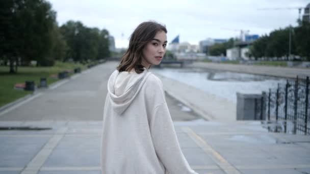 Beyaz kapüşonlu çekici esmer kız şehir limanında yürüyor. — Stok video