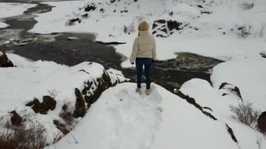 Video from the back of a girl in a beige jacket stands on top of a slope