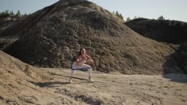 Slender girl athlete in white sportswear performs squats in nature 