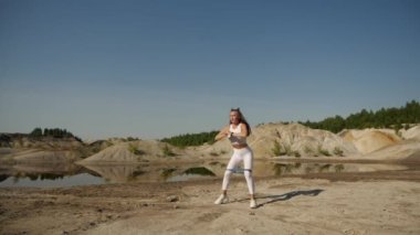 A young fit girl in a white top and white leggings, does exercises in nature 