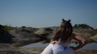 Attractive girl in white tracksuit makes lunges standing in nature 