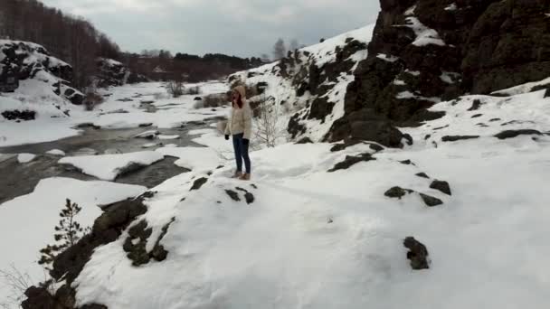 A tourist girl in a jacket stands on the slope of a snowy mountain in nature — Vídeos de Stock