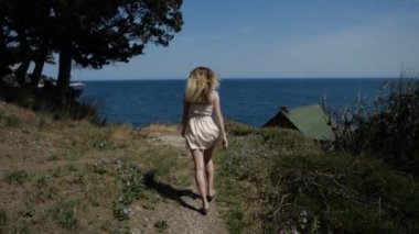 Kısa yazlık elbiseli neşeli sarışın kız yolun aşağısında ormana doğru koşuyor.