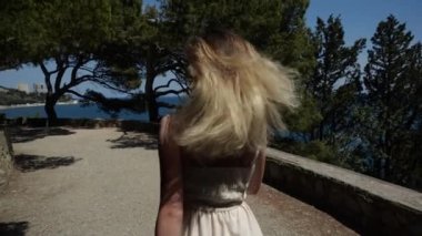 Uzun sarı saçlı bir kadın model yolun aşağısında çam ağaçlarının arasında koşuyor.