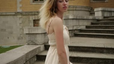 Bej elbiseli çekici bir kız fırıl fırıl döner ve doğrudan kameraya bakar.