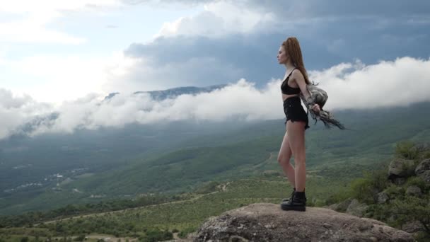 Sexy meisje in korte broek en sportieve zwarte schoenen staat op de top van de berg — Stockvideo