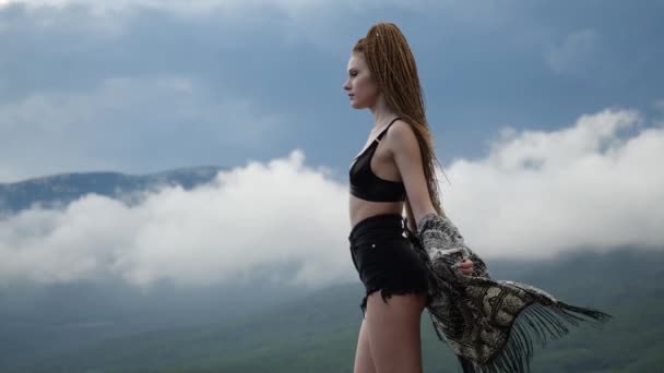 Ljusa unga brunett flicka i korta shorts och cape står högt i bergen — Stockvideo
